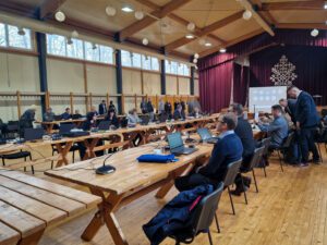 Notiek sēde, cilvēki pulcējas ap galdiem.